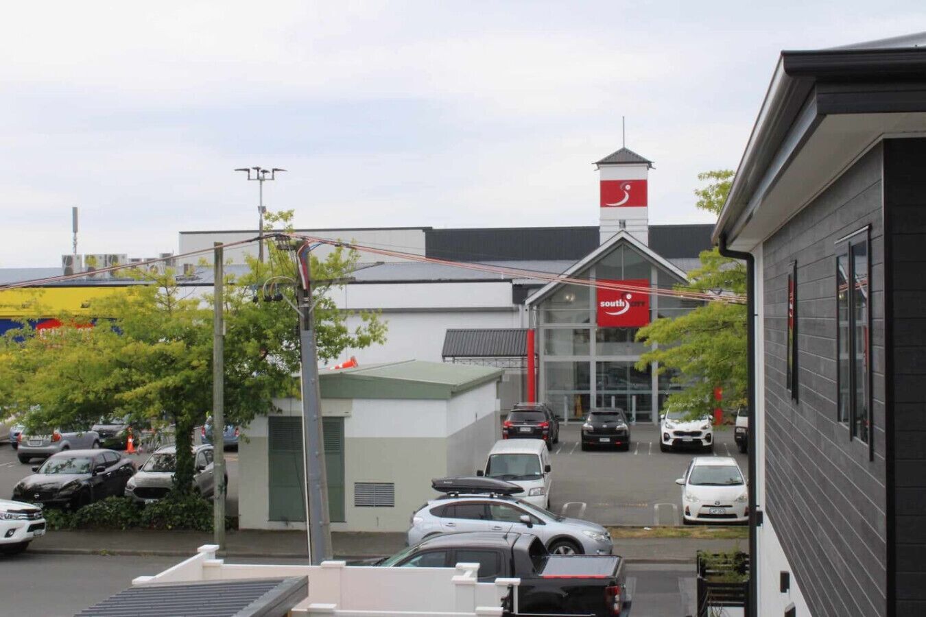 Un immeuble commercial avec une grande enseigne rouge bien visible, un parking avec plusieurs voitures et une petite tour surmontée d’un drapeau.
