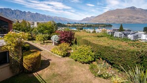 Ein Wohngebiet mit Blick auf Berge und einen See. Es sind Häuser zu sehen, ein Garten mit verschiedenen Pflanzen und ein klarer Himmel.