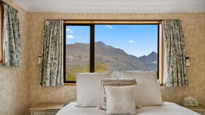 Ein Schlafzimmer mit großem Fenster und Blick auf die Berge, einem Bett mit gemusterten Kissen und Vorhängen.