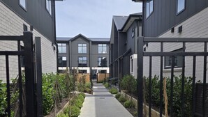 Un sendero bordeado por edificios residenciales de diseño moderno, que conduce a un edificio central con amplios ventanales.