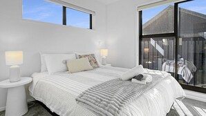 Un dormitorio con una cama grande, dos mesitas de noche y un ventanal con vistas a un edificio.