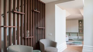 A modern living room with two grey armchairs, a wooden slatted partition, and a view into a kitchen area.