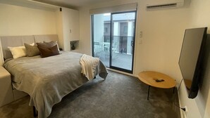 A bedroom with a bed, a small round table, a TV, and a sliding glass door to a balcony.
