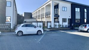 A modern building with a white facade and dark accents, featuring a covered outdoor area with a car parked in front. - Cosy Studio in Allen Street (Christchurch)