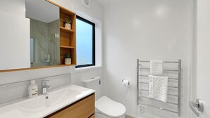 A modern bathroom with a white sink, wooden vanity, a toilet, a towel rack, and a window with a view.