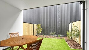 A modern indoor space with a wooden table and chairs, a green artificial turf area, and a view of a vertical garden and a wooden fence.