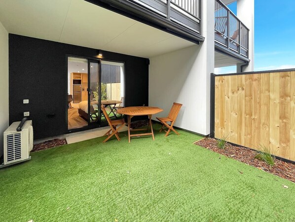 A patio with artificial grass, a wooden table and chairs, and a wooden fence.