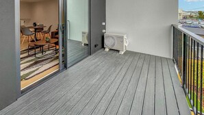 Ein Balkon mit Holzboden, eine Glastür zum Essbereich im Innenbereich und Blick auf einen Parkplatz.