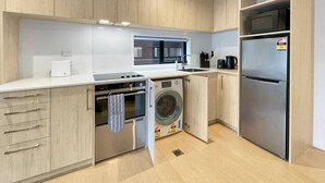 Eine moderne Küche mit Holzschränken, einem Einbauofen, einer Waschmaschine, einem Kühlschrank und einer Mikrowelle.