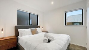 Ein modernes Schlafzimmer mit einem großen Bett, zwei Nachttischen und zwei Fenstern.