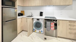 Una cocina compacta equipada con refrigerador, lavadora, horno y cafetera.