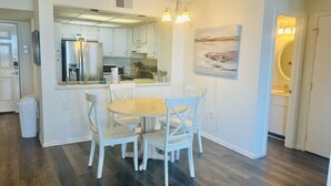 A modern kitchen with white cabinetry, a central island, and a dining area with white chairs. - 2-bedroom condo in gorgeous North Topsail Beach with WiFi, AC viewing the ocean (North Topsail Beach)