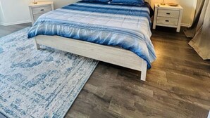 A bedroom with a bed, two bedside tables, a rug, and wall art. - 2-bedroom condo in gorgeous North Topsail Beach with WiFi, AC viewing the ocean (North Topsail Beach)
