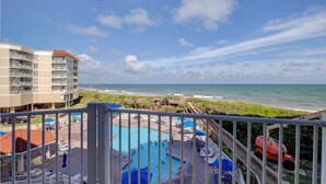 A hotel balcony with a view of the ocean, a pool area with lounge chairs, and a beach in the background. - 2-bedroom condo in gorgeous North Topsail Beach with WiFi, AC viewing the ocean (North Topsail Beach)