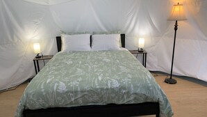 A tented accommodation with a bed, two bedside lamps, and a floor lamp.
