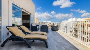 Terraza en la azotea con dos sillones de relax y una mesa de comedor, con vistas a un paisaje urbano.