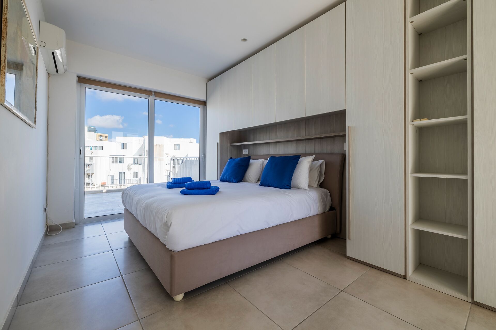 Ein modernes Schlafzimmer mit einem großen Bett, Einbauschrank und Blick auf die Stadt.