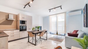 A modern kitchen with built-in appliances, a dining area with a table and chairs, and a living area with a sofa and a plant. - Stylish 2BR Escape in St Julians (Saint Julian's)