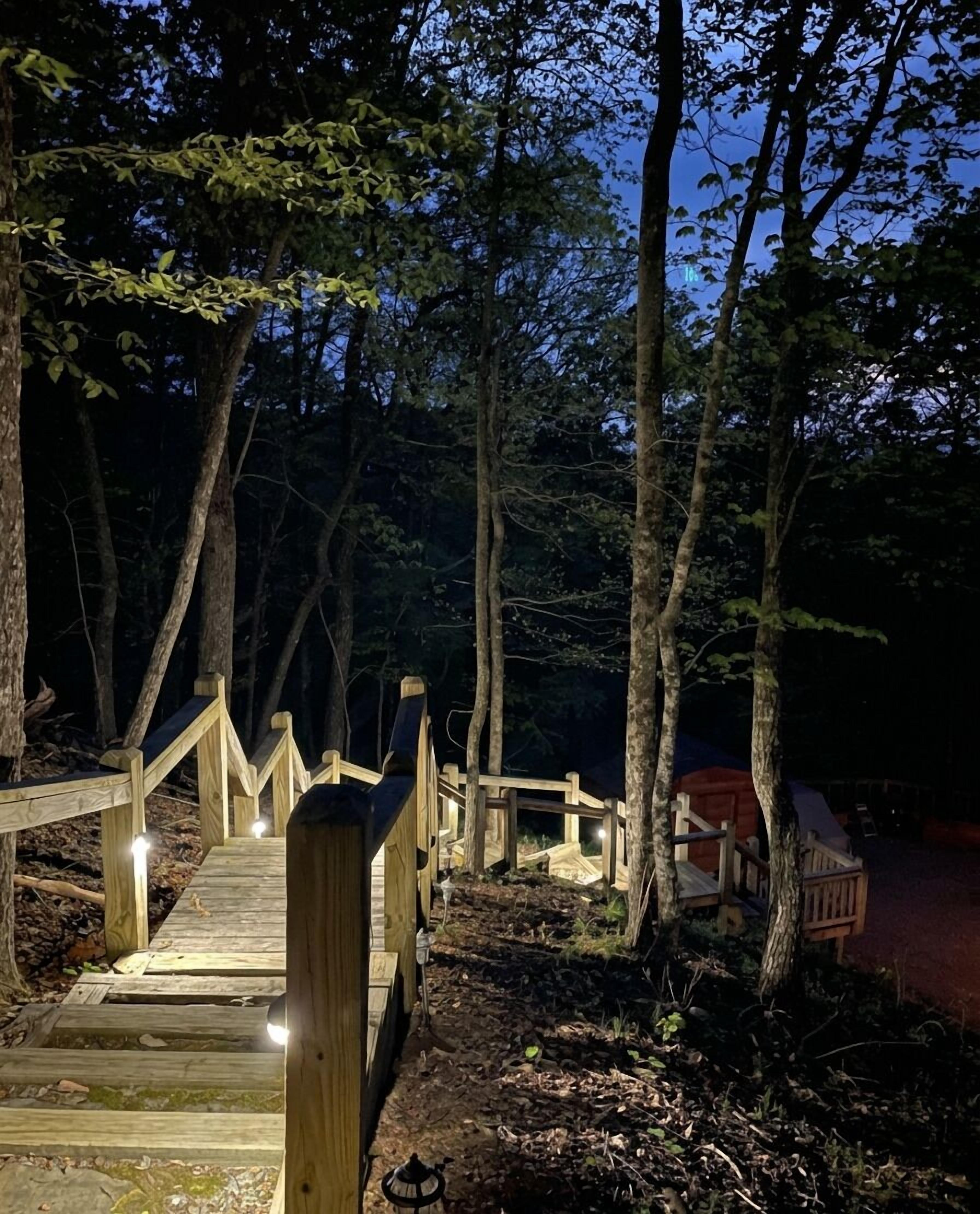 Eine Holzbrücke führt zu einem Campingplatz mit einem roten Zelt und einem kleinen Tisch.