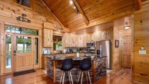 A wooden cabin interior with a kitchen island, two bar stools, and a stone accent wall. - Newly renovated  5BR 3BA Cabin with amazing Mountain Sunset views (Morganton)