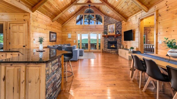 A spacious log cabin interior with a high ceiling, a stone fireplace, a dining area, and a large window overlooking the landscape. - Newly renovated  5BR 3BA Cabin with amazing Mountain Sunset views (Morganton)
