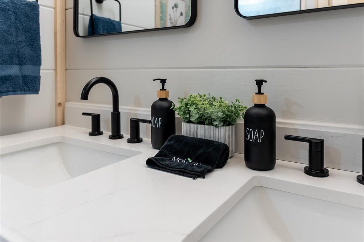 A bathroom with a white sink, black faucets, and two black soap dispensers labeled 'SOAP'.