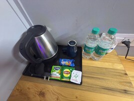 Una cafetera, dos botellas de agua Bisleri, una taza y paquetes de té sobre una superficie de madera.