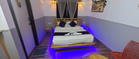 A small, cozy room with a bed, a nightstand, a wooden bench, and a red chair.