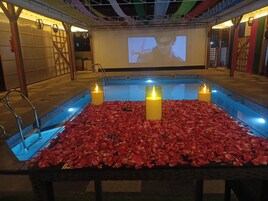 Un área de piscina con pétalos de rosa y velas, una pantalla de proyección y una terraza de madera.