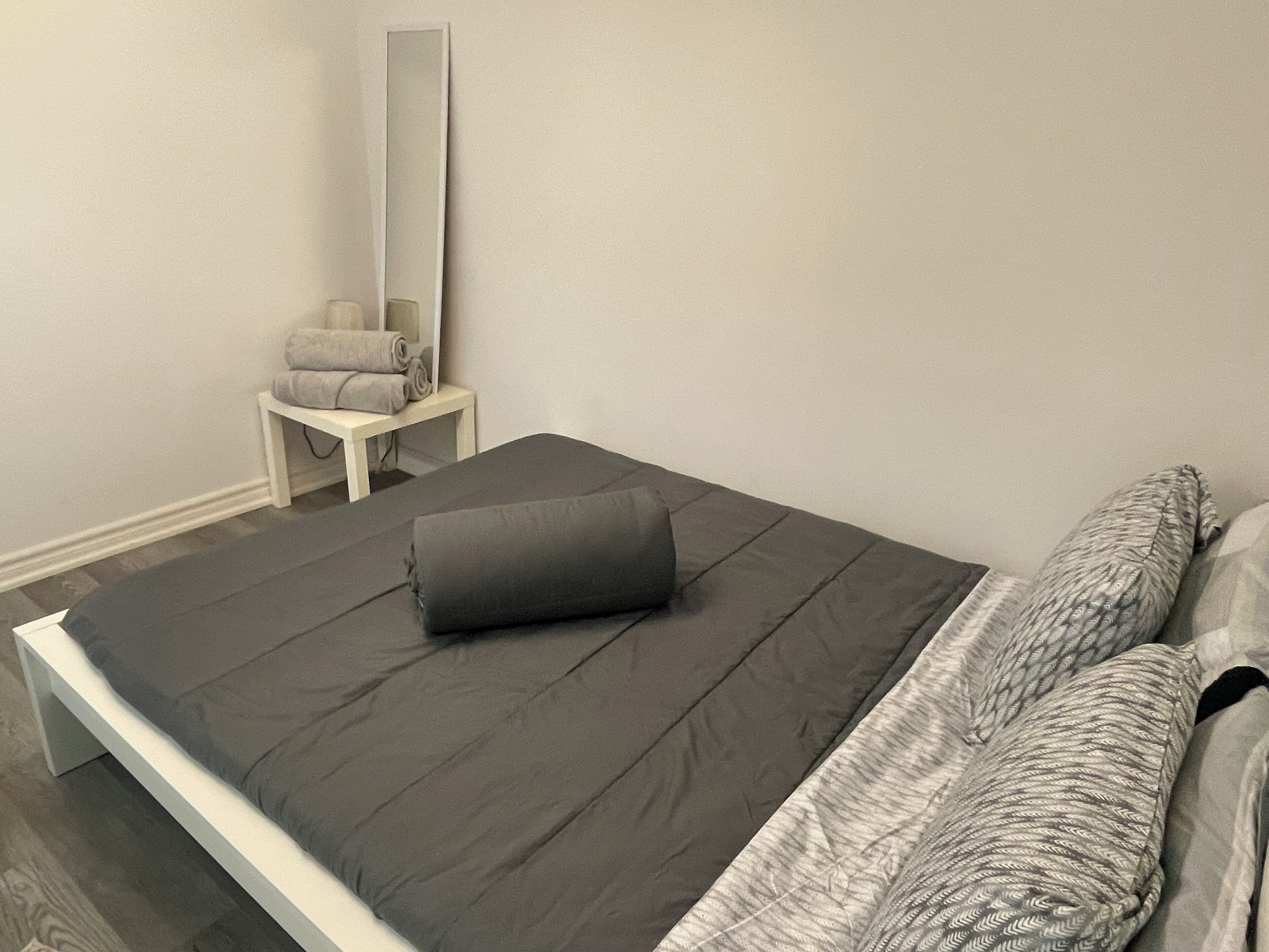 A bedroom with a bed, a bedside table with a rolled towel, and a mirror on the wall.