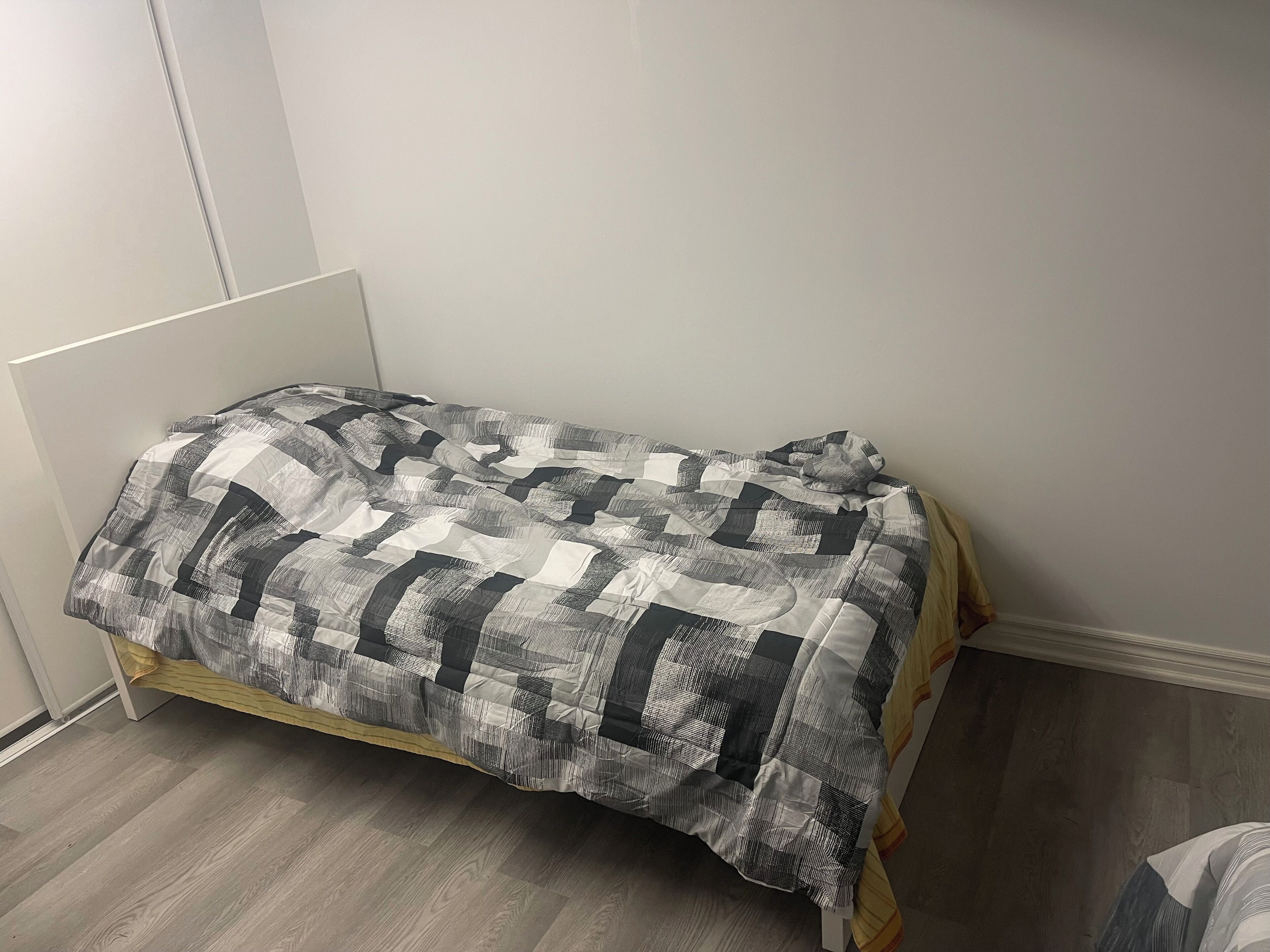 A single bed with a quilted blanket in a room with wooden flooring and white walls.