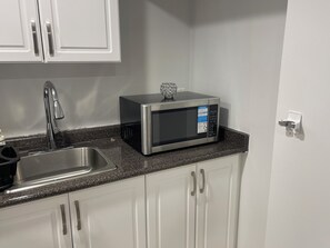 Una cocina con un lavamanos de acero inoxidable, un microondas y gabinetes blancos.