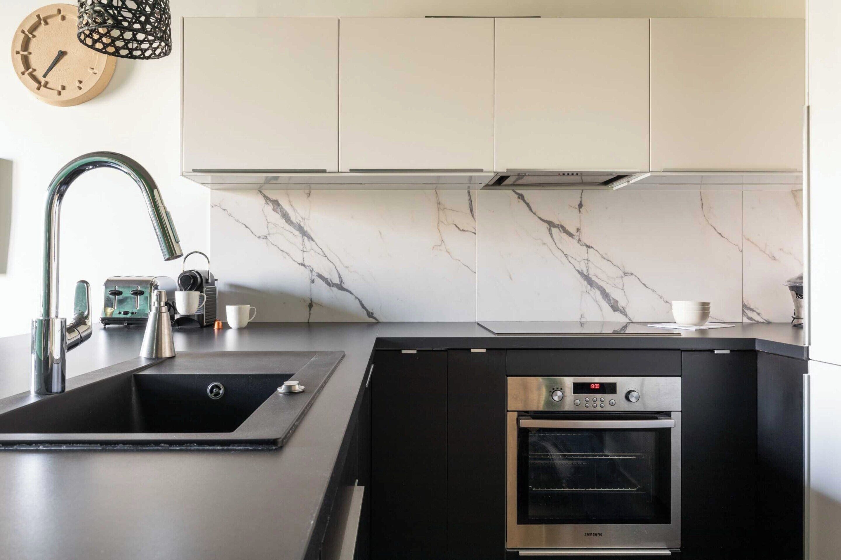 A modern kitchen with a built-in oven, stainless steel sink, and a marble backsplash.