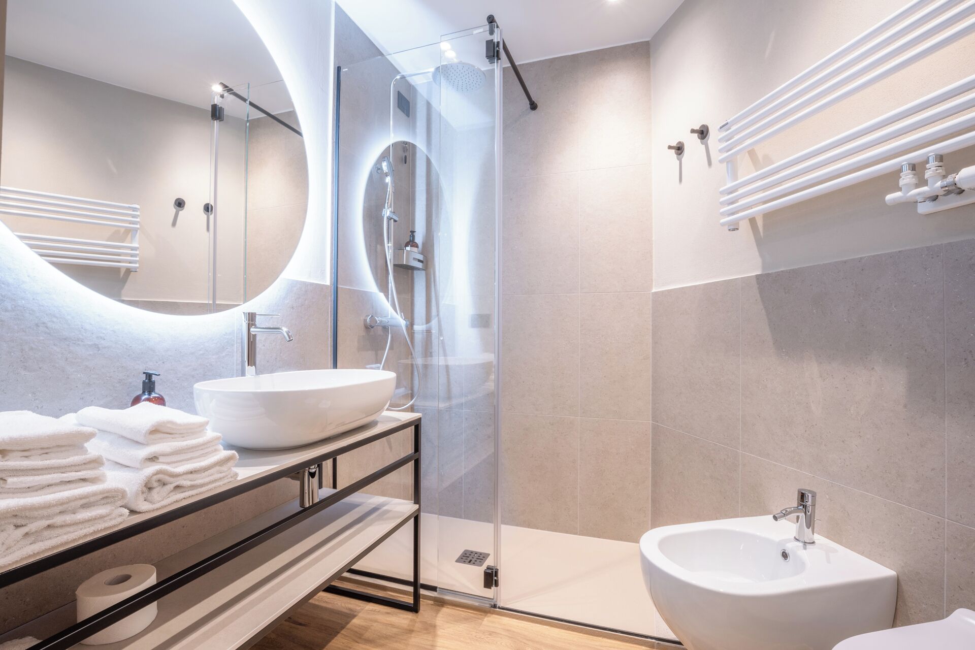Un baño moderno con ducha de vidrio, tocador con espejo grande y lavamanos separado.