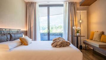 Una habitación de hotel con una cama, un banco, una mesa con un florero y vistas a zonas verdes por la ventana.
