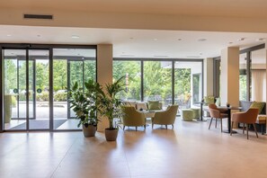 A spacious indoor area with large windows, potted plants, and modern furniture. - Alchimia WellResort (Ponte Arche)