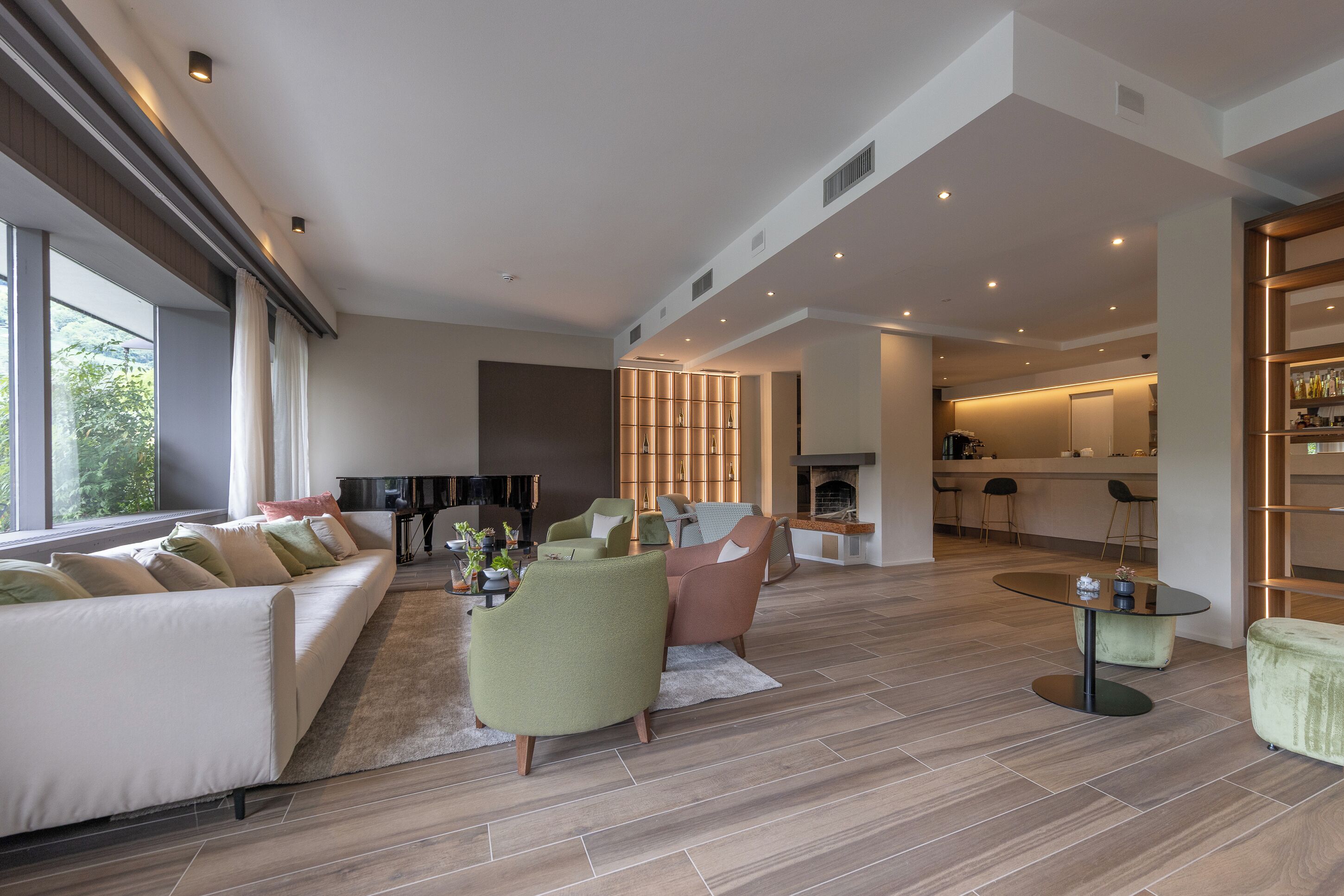 Een ruime zithoek met een bank, fauteuils, een salontafel, en een keuken op de achtergrond.