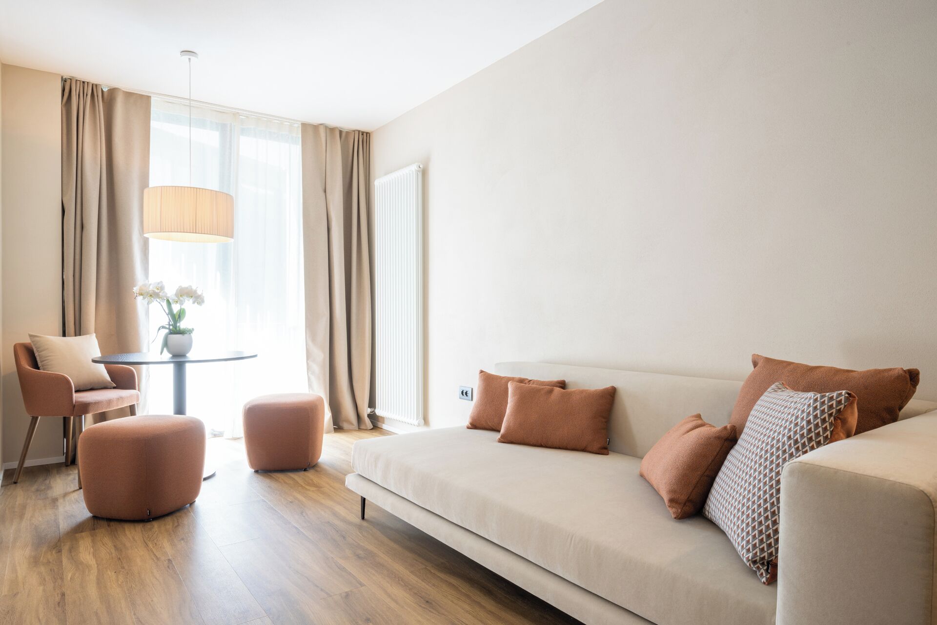 Uma sala de estar moderna com sofá, apoio para os pés, poltrona e uma mesa com abajur e flores.