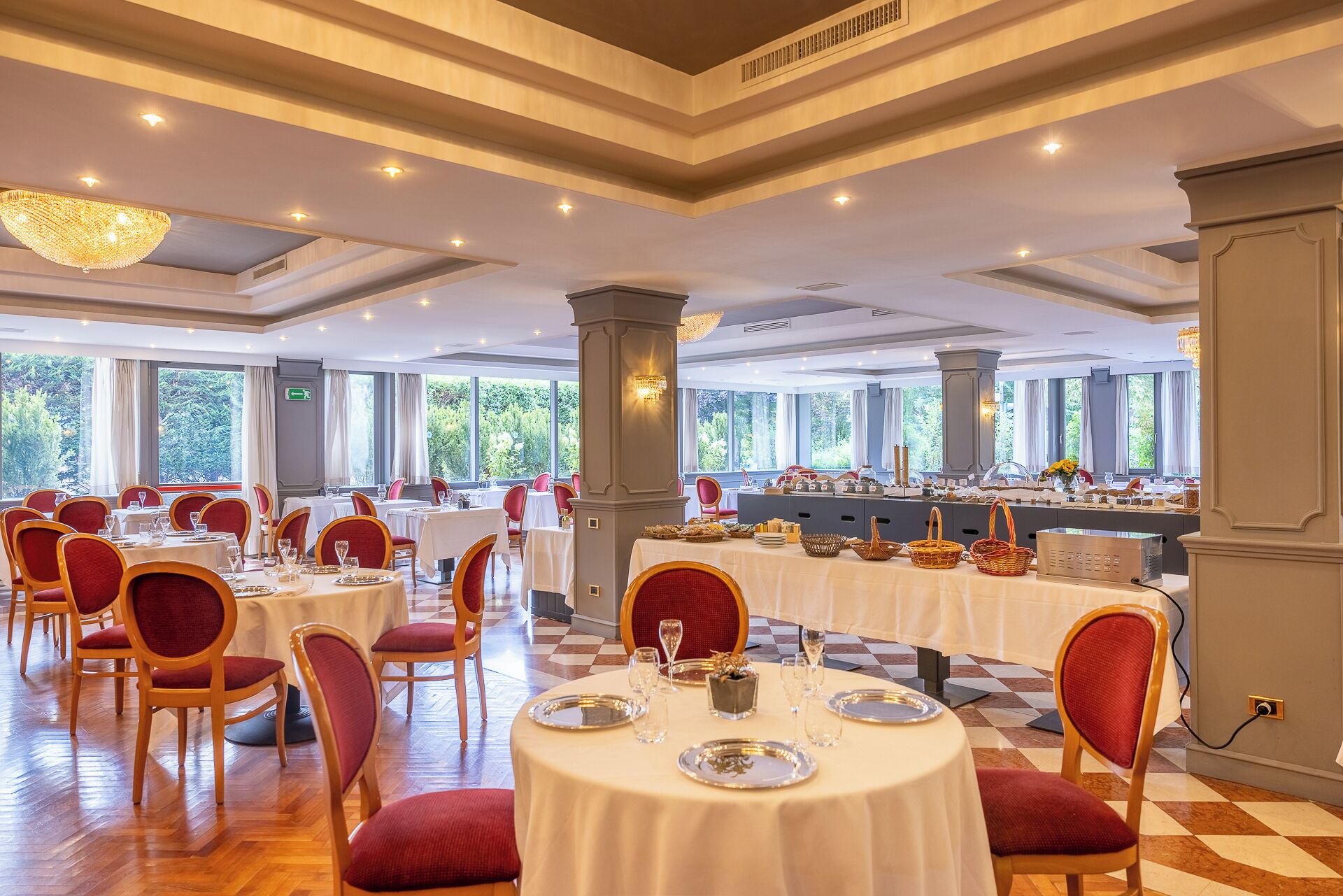 Uma ampla sala de jantar com mesas redondas, cadeiras estofadas em vermelho e um buffet.