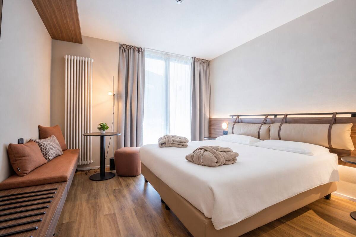 Una camera d'albergo moderna con un letto grande, un'area salotto, un tavolino con una pianta e un termosifone.