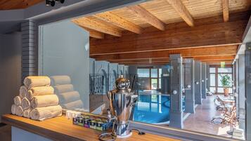 Une chambre d’hôtel avec un plafond en bois, un grand miroir reflétant l’espace piscine, et un comptoir avec des serviettes et des tasses à thé.