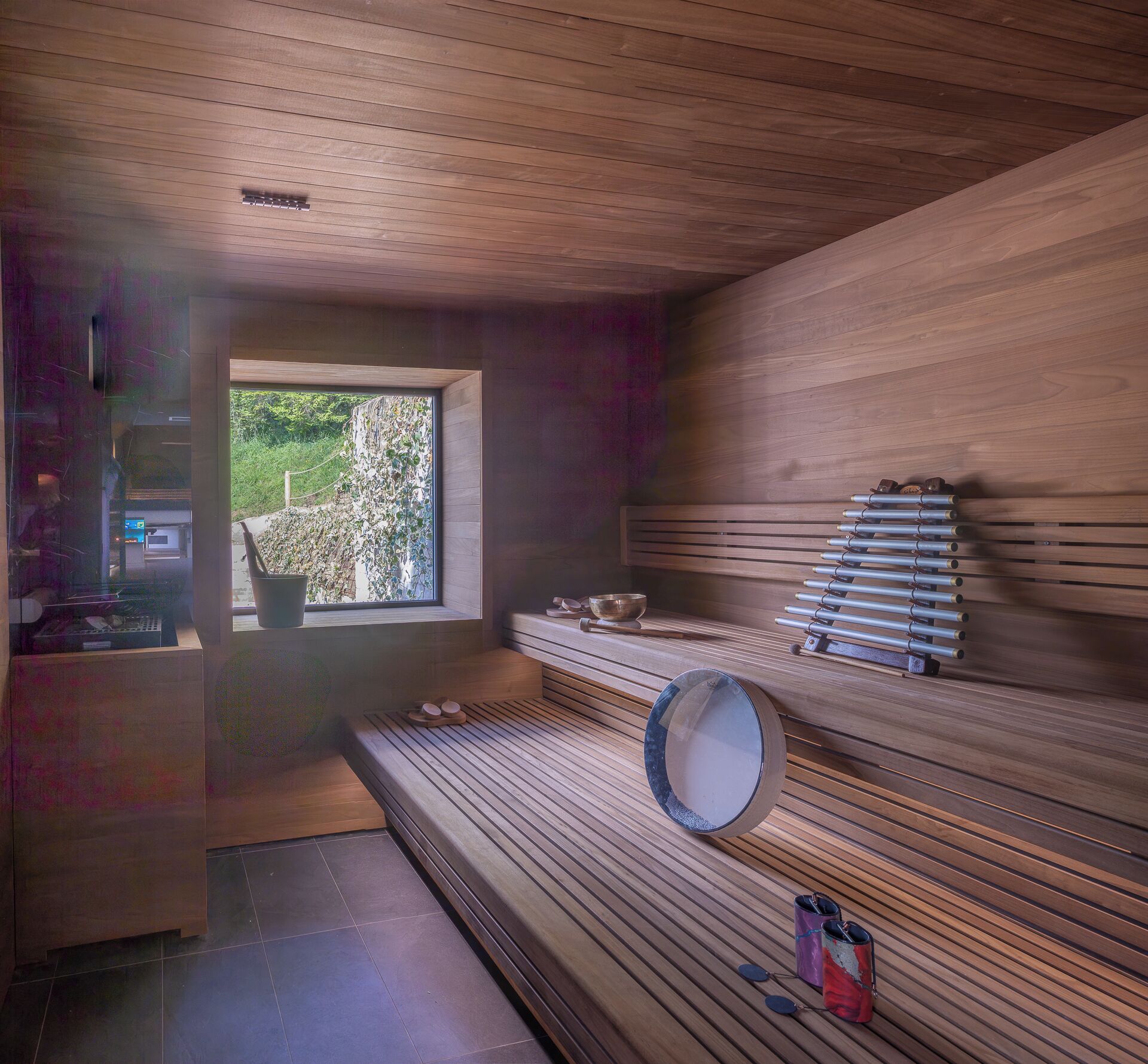 A sauna room with wooden benches, a large mirror, and a window providing a view of greenery outside.