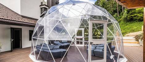 Estructura en forma de cúpula geodésica con asientos en su interior, ubicada sobre una terraza de madera.