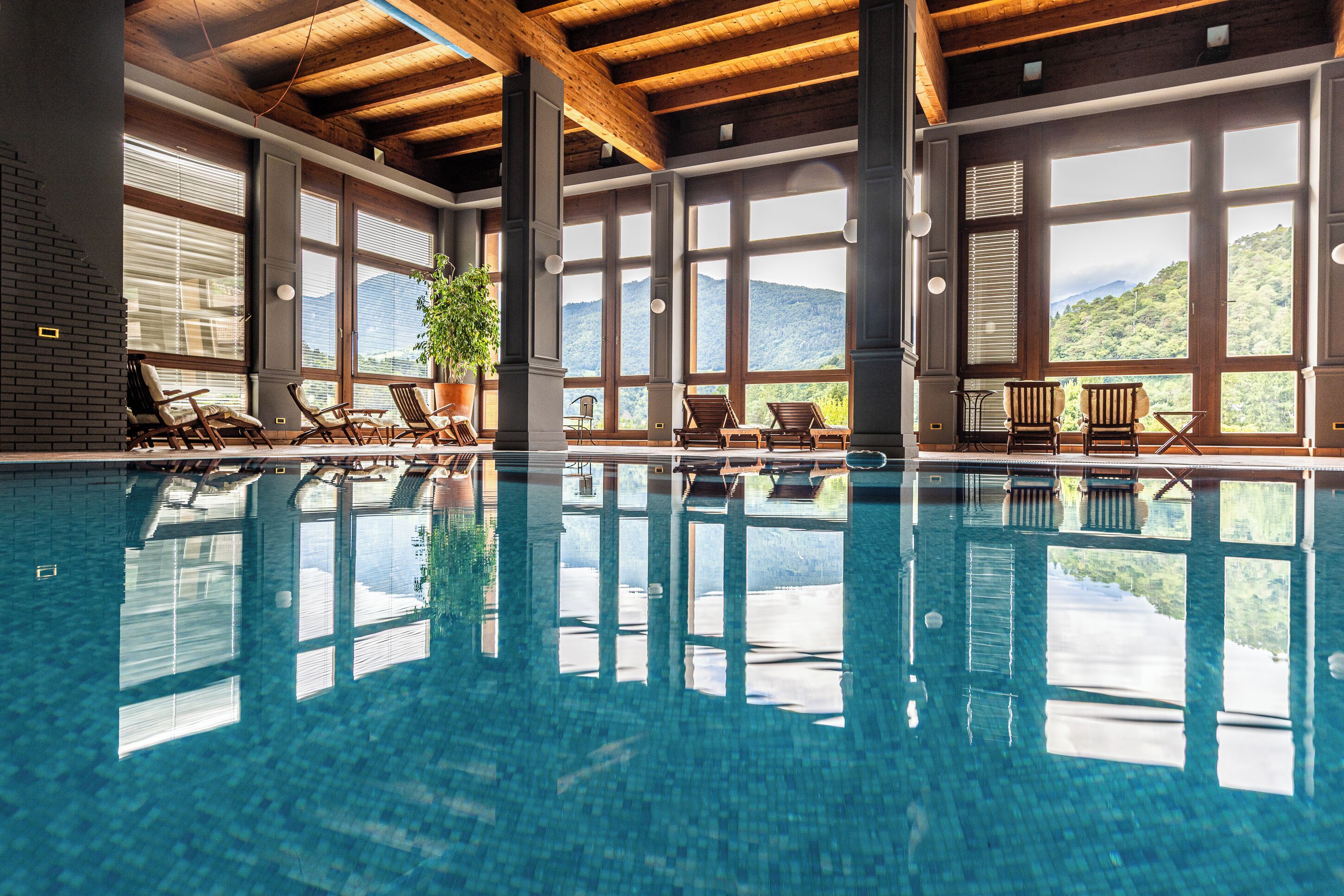 A swimming pool with clear blue water, wooden beams, and large windows offering mountain views.