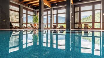 A swimming pool with clear blue water, wooden beams, and large windows offering mountain views.