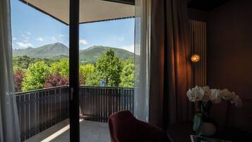 A balcony with a view of mountains and greenery, a red chair, a table with a vase of flowers, and a remote control.