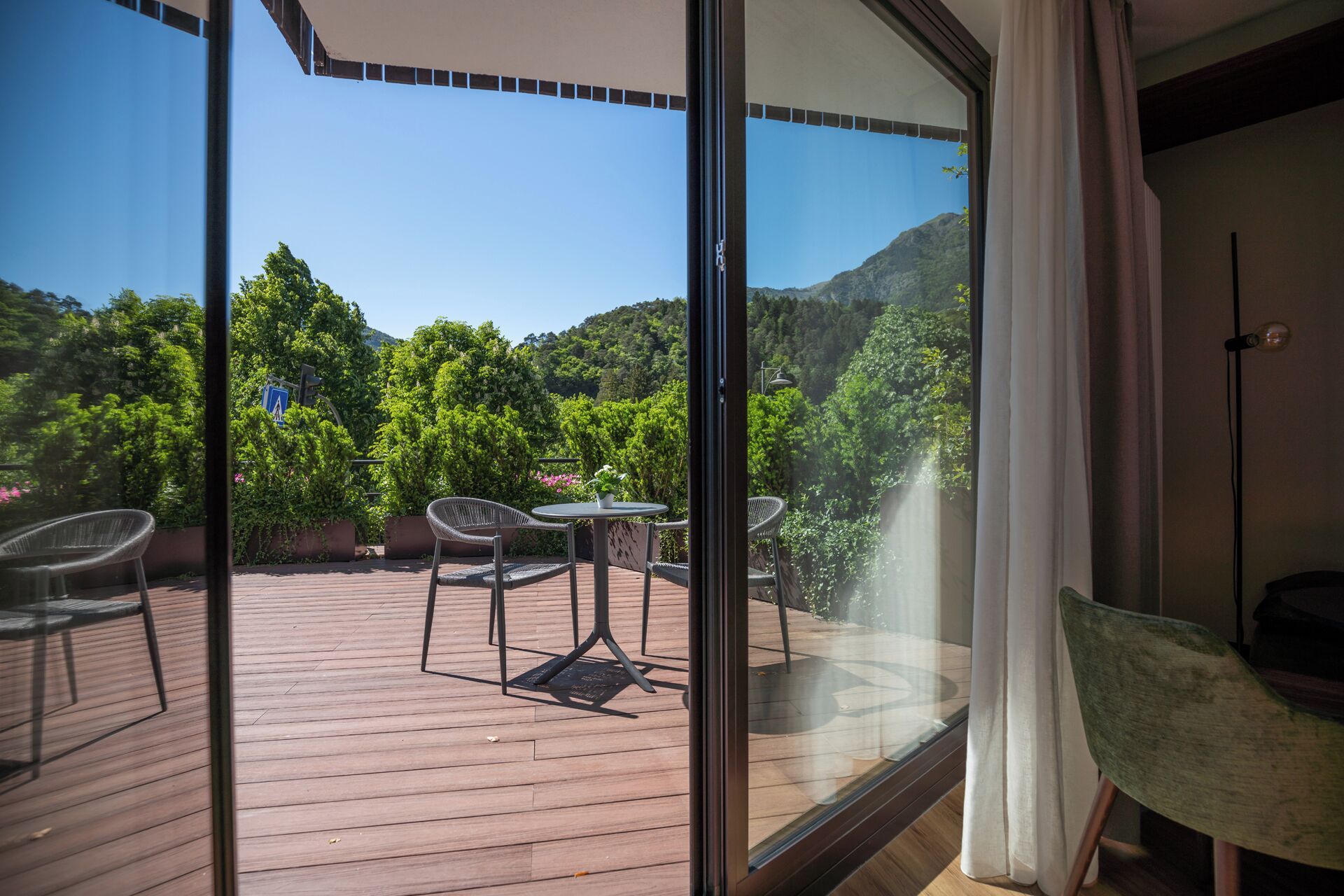 A balcony with a wooden deck, two chairs, a small table, and a view of a mountainous landscape.