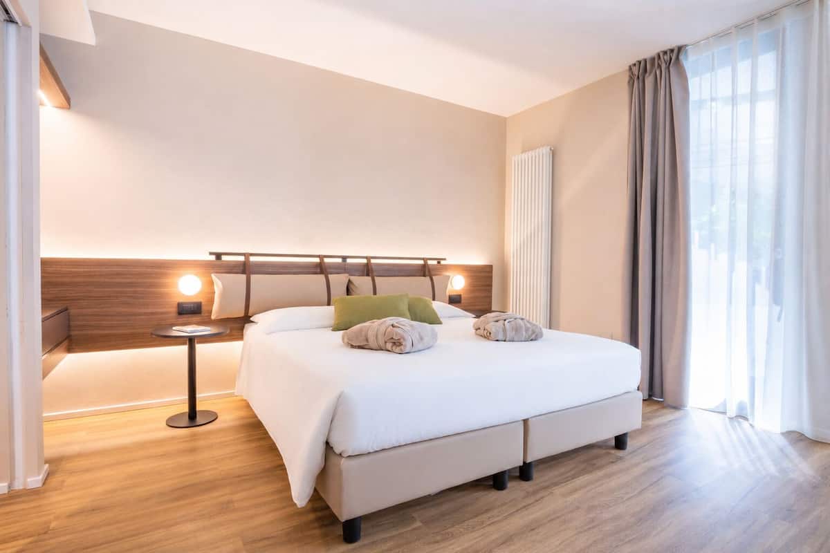 Camera d'albergo con un letto grande, comodini, un termoriscalfatore e una finestra con tende.