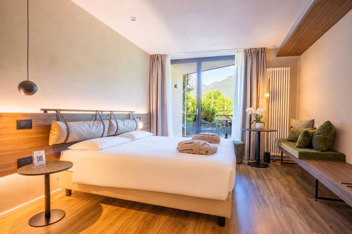Una camera d'albergo moderna con un letto grande, un tavolino, una poltrona e vista sul verde.