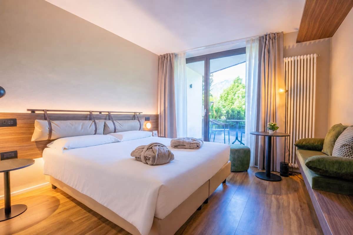 Una camera d'albergo con un letto grande, un tavolino, un divano verde e vista sul verde circostante.